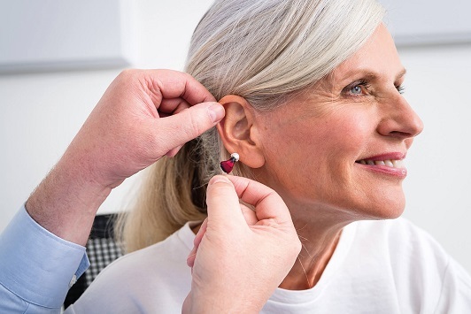 Ältere Frau bekommt ein modernes Hörgerät angepasst, Hörakustik und Seniorenhilfe.